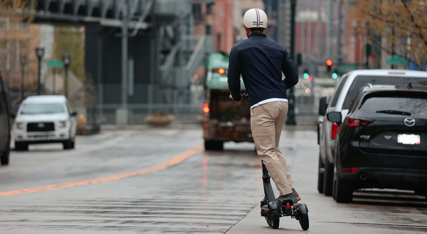 Una persona en patinete eléctrico baja por una calle mojada.