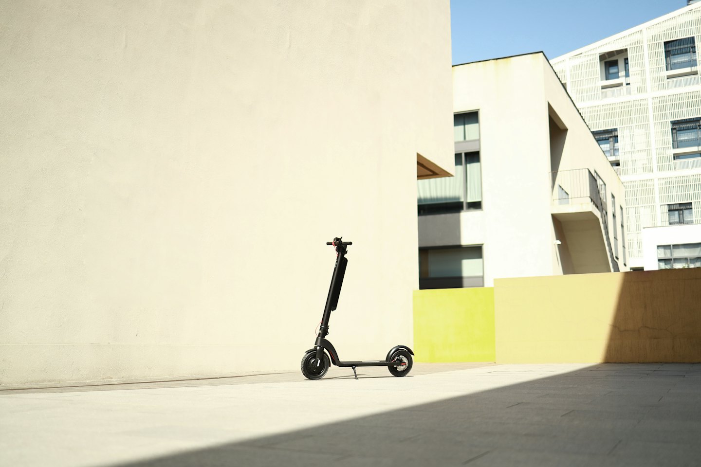 Patinete eléctrico negro aparcado junto a una pared de hormigón con edificios modernos.